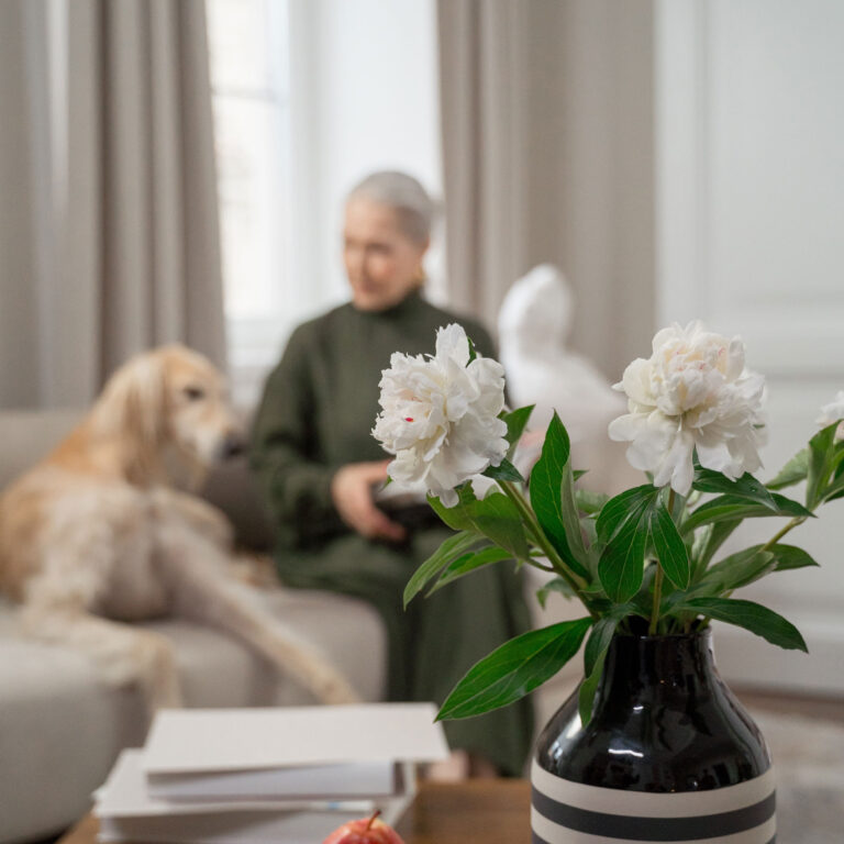flowers in a vase with a woman and a dog in the background